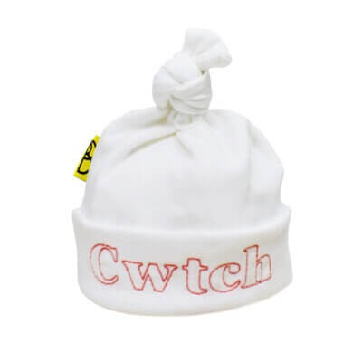 Handmade white Welsh organic cotton baby hat embroidered with word Cwtch in red and made in Wales