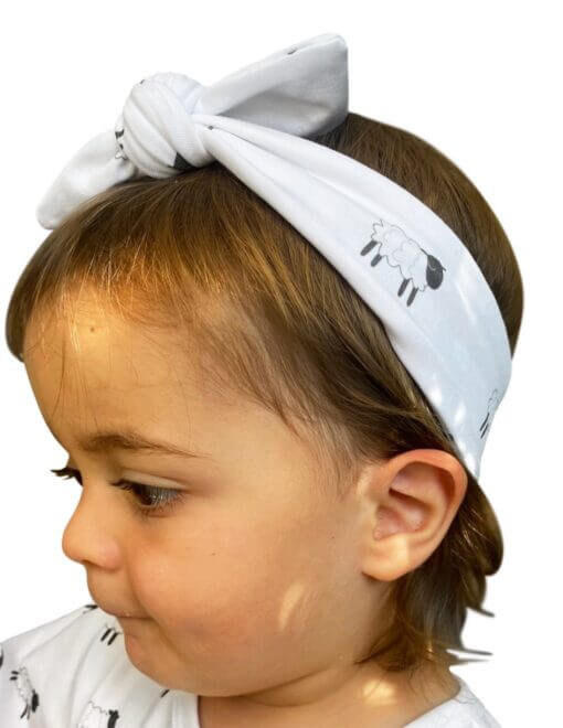 Organic cotton headband around the top of her head, with a bow in our black and white leaping lambs print. Made from GOTs certified organic cotton.