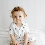 Organic cotton baby sleepsuit with hand drawn cute leaping lambs pattern printed on white organic cotton. Onesie has nickel-free poppers around crotch