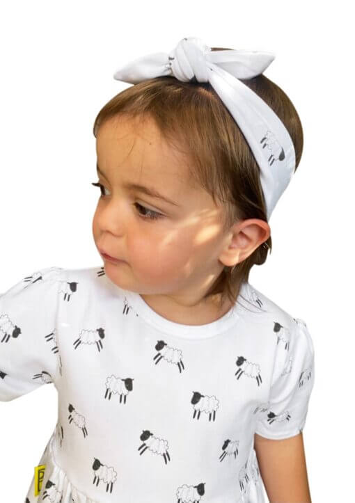 Organic cotton headband around the top of her head, with a bow in our black and white leaping lambs print. Made from GOTs certified organic cotton.