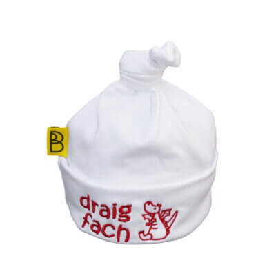 Handmade white Welsh organic cotton baby hat embroidered with a red dragon and words Draig Fach in red. Made in Wales.