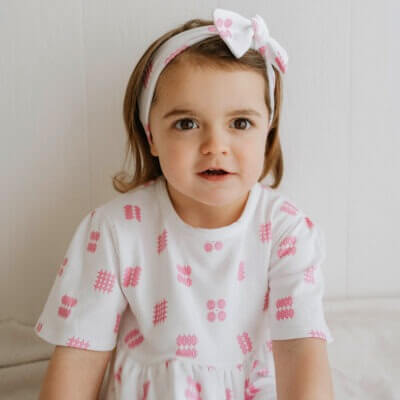 Infants handmade white organic cotton headband with a bow in pretty pink tapestry design