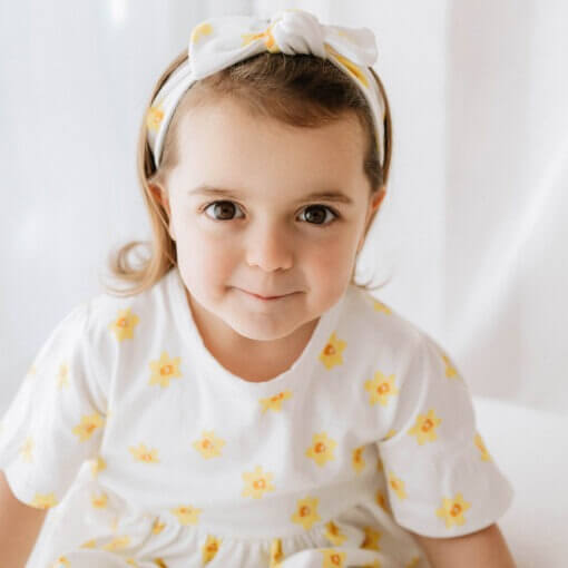 Infants handmade white organic cotton headband with a bow in a vibrant daffodil design