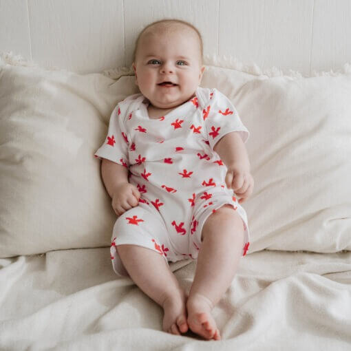 White short sleeved handmade organic cotton baby romper in cute red dragons design with fasteners at bottom for easy opening