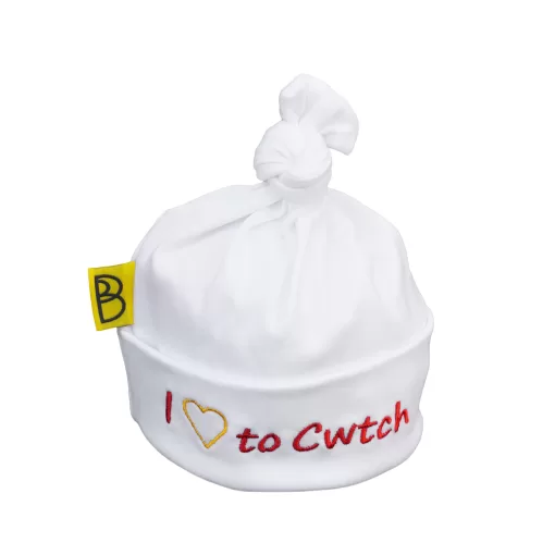 Handmade white Welsh organic cotton baby hat embroidered with words I Love to Cwtch in red and a yellow embroidered heart instead of the word love